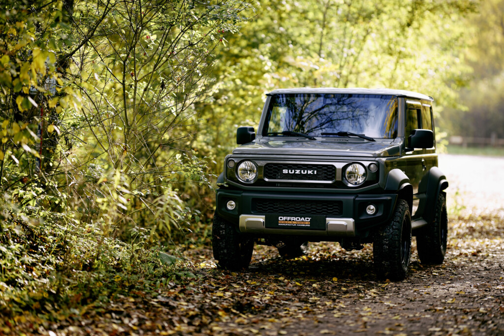 Grüner Suzuki Jimny, Frontansicht auf einem herbstlichen Waldweg