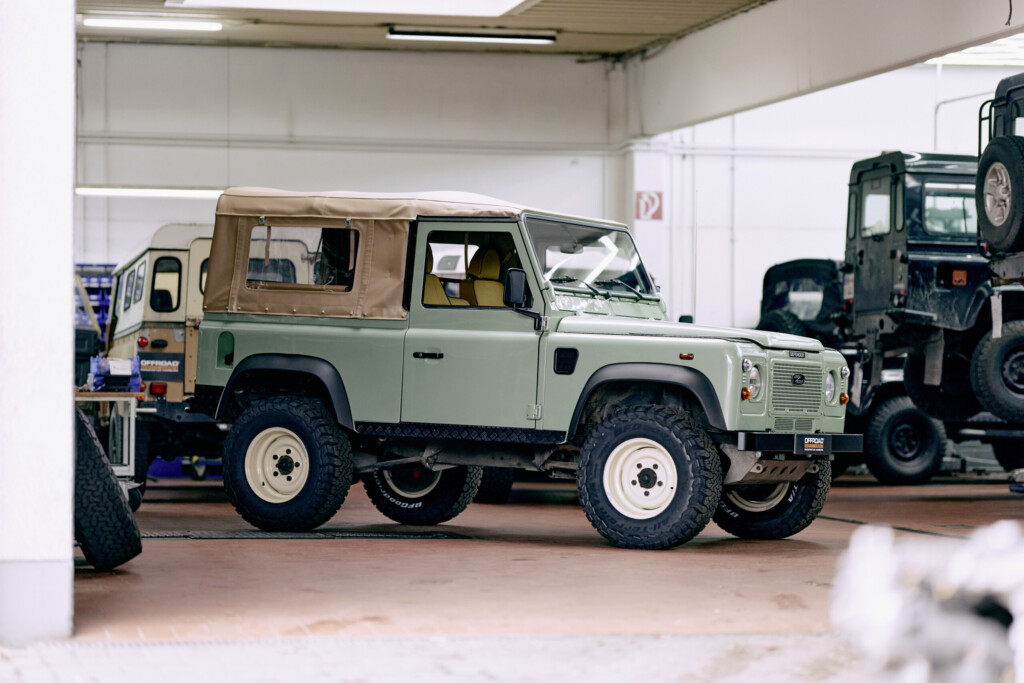 Restaurierter Land Rover Defender 90 in Heritage-Grün mit beigem Verdeck in der Werkstatt der Offroad Manufaktur Hamburg