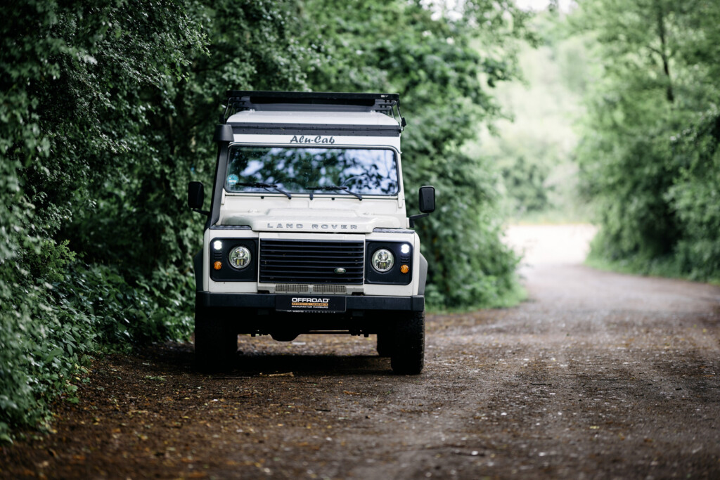 Land Rover Defender 110 in Weiß auf Waldweg, Frontansicht