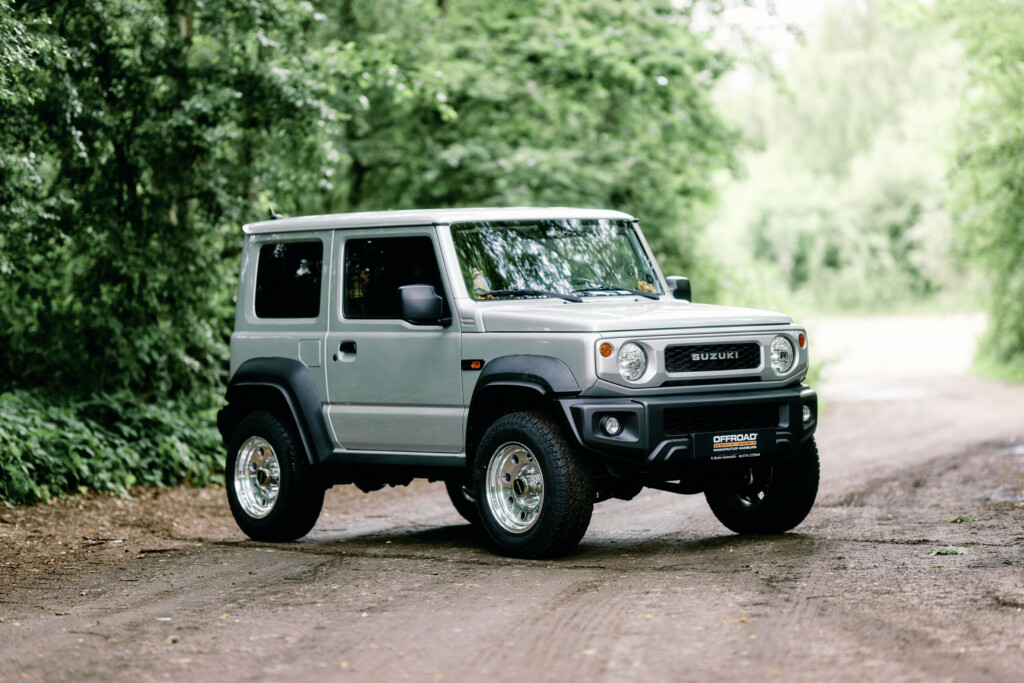 Suzuki Jimny HJ in Silber, höhergelegt, auf Waldweg – Frontansicht