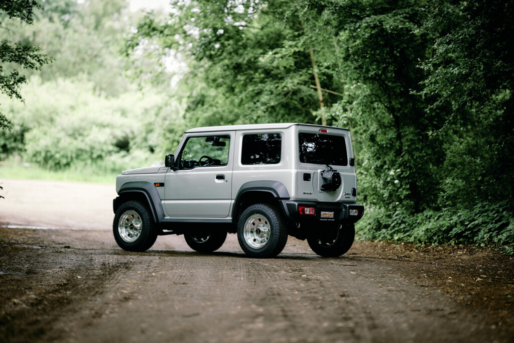 Suzuki Jimny HJ frontal auf Schotterweg im Wald