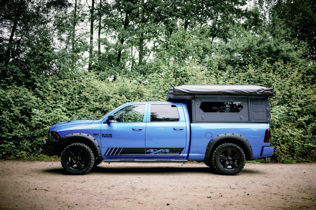 Blue Dodge RAM 1500 with Alu-Cab ModCAP camper conversion, side view on a forest track