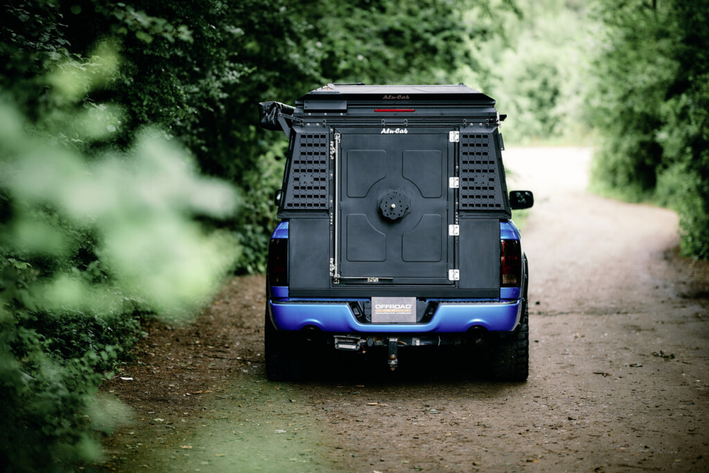 Dodge RAM 1500 mit Alu-Cab ModCAP Aufbau, Heckansicht auf schmalem Waldweg