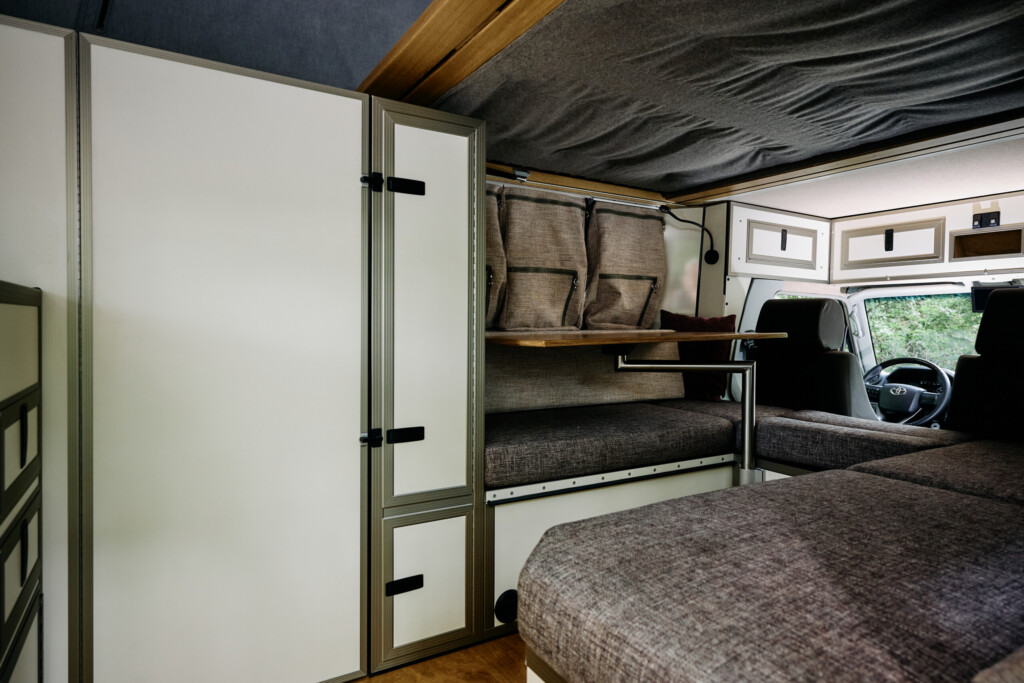 Innenraum des Camper-Aufbaus mit Sitz- und Schlafbereich, Blick nach vorn