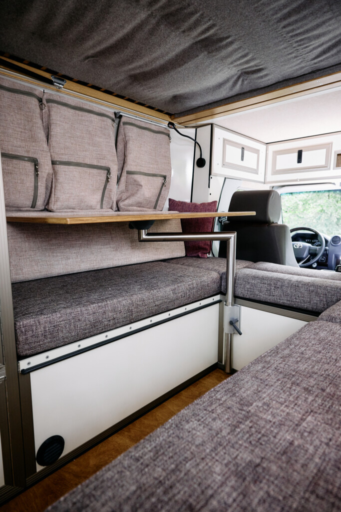 Wohnbereich im Camper-Aufbau mit Polstern, Stauraumtaschen und Tisch