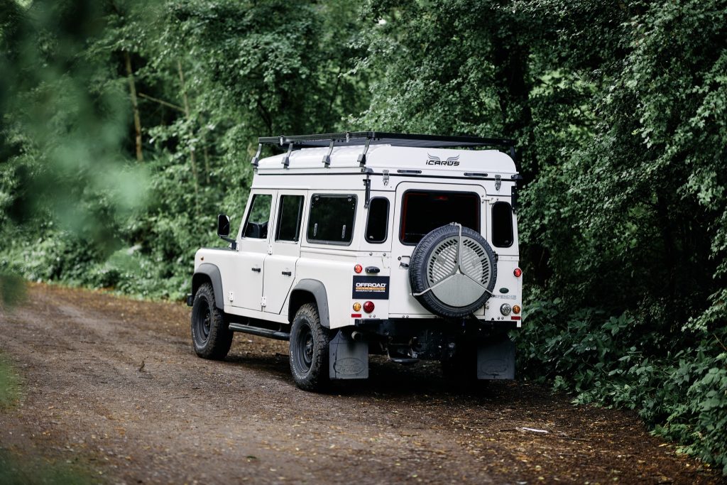 Land Rover Defender 110 mit eingeklapptem Hubdach auf dem Waldweg, schräg von hinten