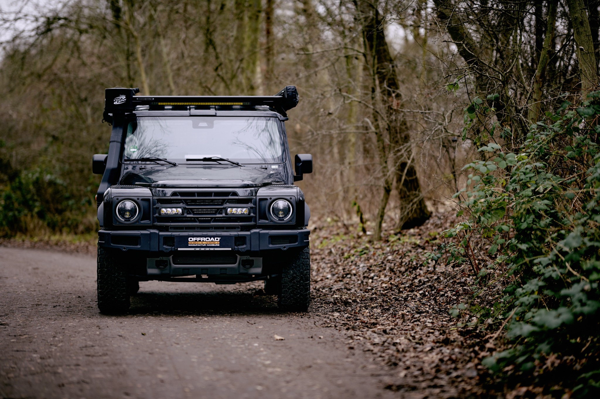 INEOS Grenadier in Schwarz frontal auf einem Waldweg mit Lazer Zusatzscheinwerfern