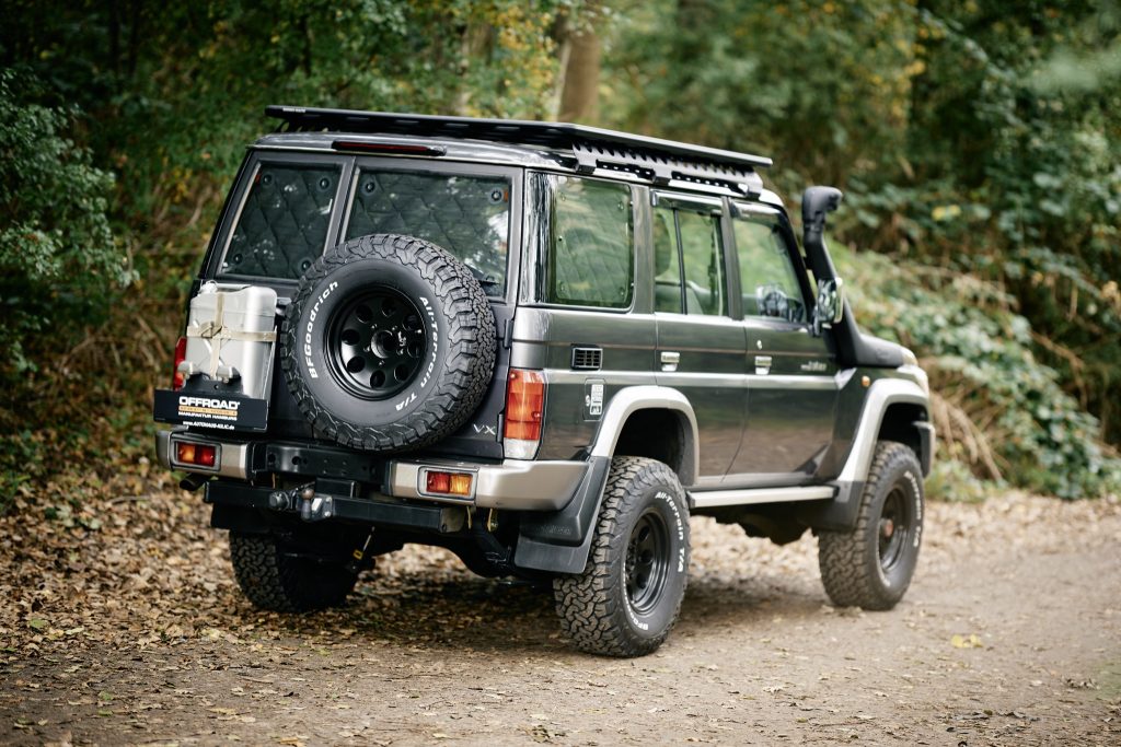 Toyota Land Cruiser GRJ76 mit Dachträger und Reserverad, schräg von hinten im Wald