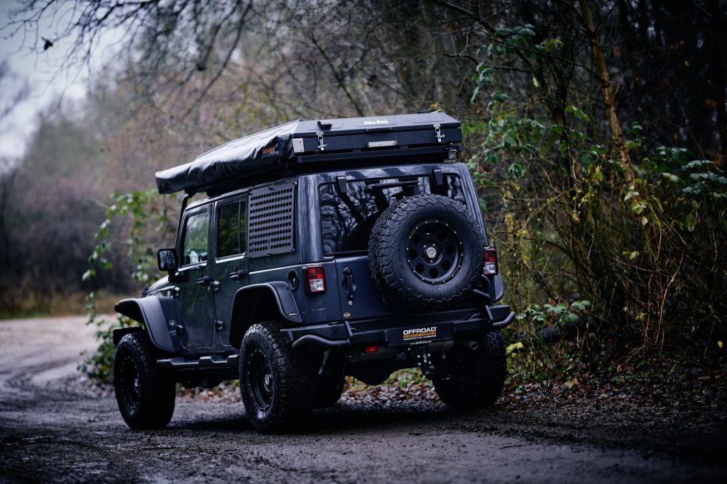 Jeep Wrangler JKU mit Alu-Cab Dachzelt und Reserverad, schräg von hinten im Wald