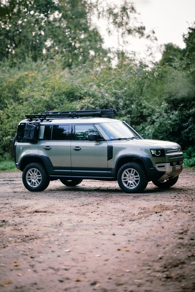 New Defender 110 von der Seite auf einem Waldweg