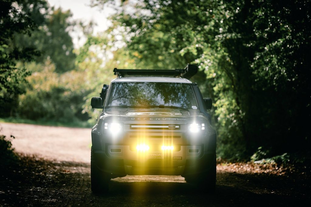 New Defender 110 im Wald mit Fernlicht und Lazer-Zusatzlicht